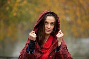 Retrato de una mujer en impermeable rojo con capucha caminando en el parque en un día lluvioso foto