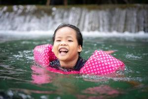 Little Asian girl wearing inflatable sleeves swimming in nature water on holiday photo