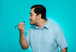 Young man blowing glasses in hand on blue background photo