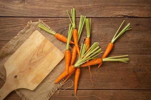 zanahorias frescas frescas sobre tabla de cortar de madera y fondo de madera foto