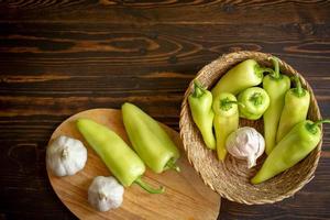 Green hot chili peppers and garlic in the basket on wooden background