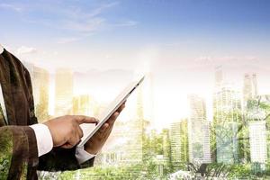Double exposure of success businessman using tablet with city landscape background. Nature and Building construction. Mixed media photo