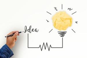 Creativity inspiration, ideas and innovation concepts with lightbulb and paper crumpled ball. Hand of businessman writing text idea with pen. photo