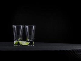 Dos tragos de tequila vacíos con jugosa lima sobre un fondo oscuro foto