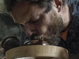 man with a beard breathes smoke into a traditional teapot photo