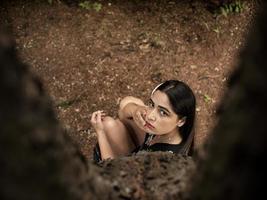 Attractive girl of Caucasian appearance sitting near a tree, holding a hand near the face. view from above photo