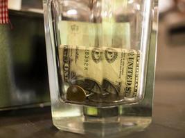 un dólar y monedas en un vaso de vidrio facetado foto