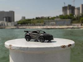 Modelo de coche de juguete en negro con el telón de fondo del mar y edificios de gran altura foto