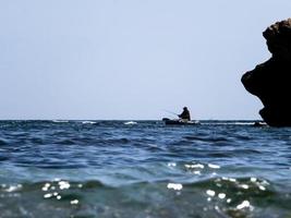 Pescador en un bote inflable en el mar contra el cielo azul foto