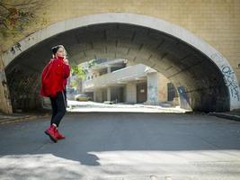 young hipster girl in a knitted hat and red boots walking down the street under the bridge photo