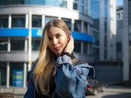 Retrato de una hermosa niña en una chaqueta de mezclilla en el fondo de un moderno centro de negocios en un día soleado foto