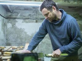 woodworker with a beard sawing a wooden beam with a hand saw. a carpenter sawing a piece of wood photo