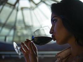 Retrato de una chica atractiva con hermosos labios que bebe vino tinto de una copa foto