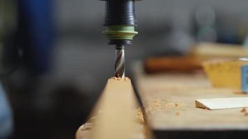 carpintero perfora un agujero en una tabla de madera con un taladro. video