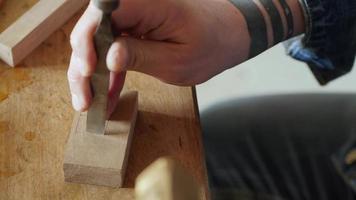 le menuisier découpe un trou carré sur la planche avec un ciseau. sculpture sur bois dans un atelier de menuiserie. l'art du travail du bois. le son des outils de menuiserie à main
