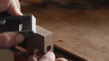 A carpenter removes chamfer from a piece of wood with a small plane