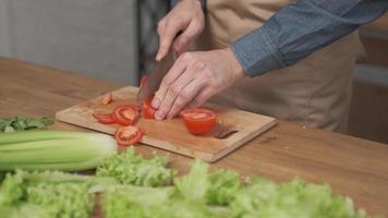 Primer plano de manos de hombre cortando verduras en tabla de cortar de madera para ensalada en la mesa con comida sana en la cocina. foto