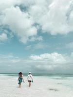 Vista posterior de la feliz pareja joven caminando por una playa tropical desierta con un cielo azul claro brillante