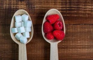 Healthy raspberries and uhealthy sugar in wooden spoons