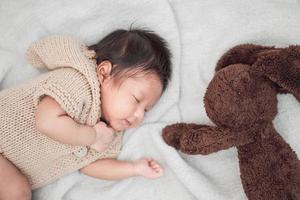 Adorable bebé recién nacido durmiendo pacíficamente con muñeca de conejo marrón sobre una manta blanca foto