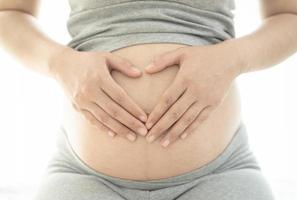 Close up of pregnant woman making heart shape hand sign on her bare tummy photo