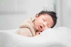 Newborn baby boy sleeping and wearing a silver crown photo