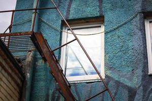 White window in blue textured wall with rusty metal stairs underneath photo
