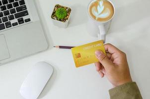 Top view man holding a credit card and on the desk. Laptop computer Notepad and pen.Online shopping business, pay by credit card photo