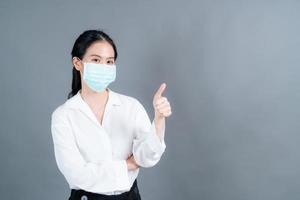Joven mujer asiática con mascarilla médica y dando pulgares hacia arriba