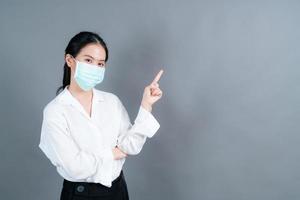 Joven asiática vistiendo mascarilla médica y señalar con el dedo