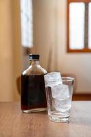 Ice cube in glass with cold brew coffee on wood table photo