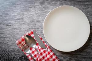 Empty plate or dish with knife, fork, and spoon on wood tile background photo