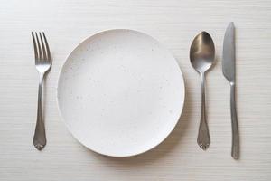 Empty plate or dish with knife, fork, and spoon on wood tile background photo