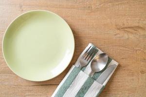 Empty plate or dish with knife, fork, and spoon on wood tile background photo