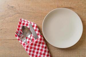 Empty plate or dish with knife, fork, and spoon on wood tile background photo