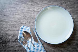 Empty plate or dish with knife, fork, and spoon on wood tile background photo