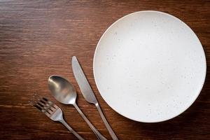 Empty plate or dish with knife, fork, and spoon on wood tile background photo