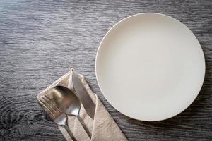 Empty plate or dish with knife, fork, and spoon on wood tile background photo