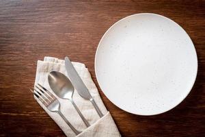 Empty plate or dish with knife, fork, and spoon on wood tile background photo