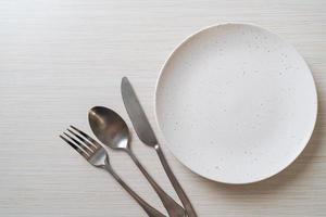 Empty plate or dish with knife, fork, and spoon on wood tile background photo