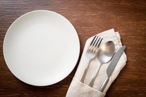 Empty plate or dish with knife, fork, and spoon on wood tile background photo