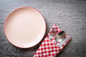 Empty plate or dish with knife, fork, and spoon on wood tile background photo