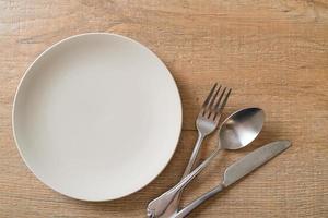 Empty plate or dish with knife, fork, and spoon on wood tile background photo