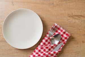 Empty plate or dish with knife, fork, and spoon on wood tile background photo