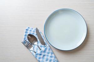 Empty plate or dish with knife, fork, and spoon on wood tile background photo