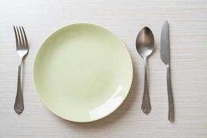 Empty plate or dish with knife, fork, and spoon on wood tile background photo