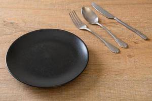 Empty plate or dish with knife, fork, and spoon on wood tile background photo