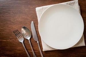 Empty plate or dish with knife, fork, and spoon on wood tile background photo