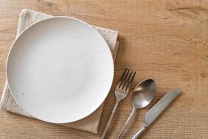 Empty plate or dish with knife, fork, and spoon on wood tile background photo