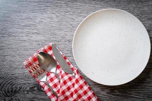 Empty plate or dish with knife, fork, and spoon on wood tile background photo